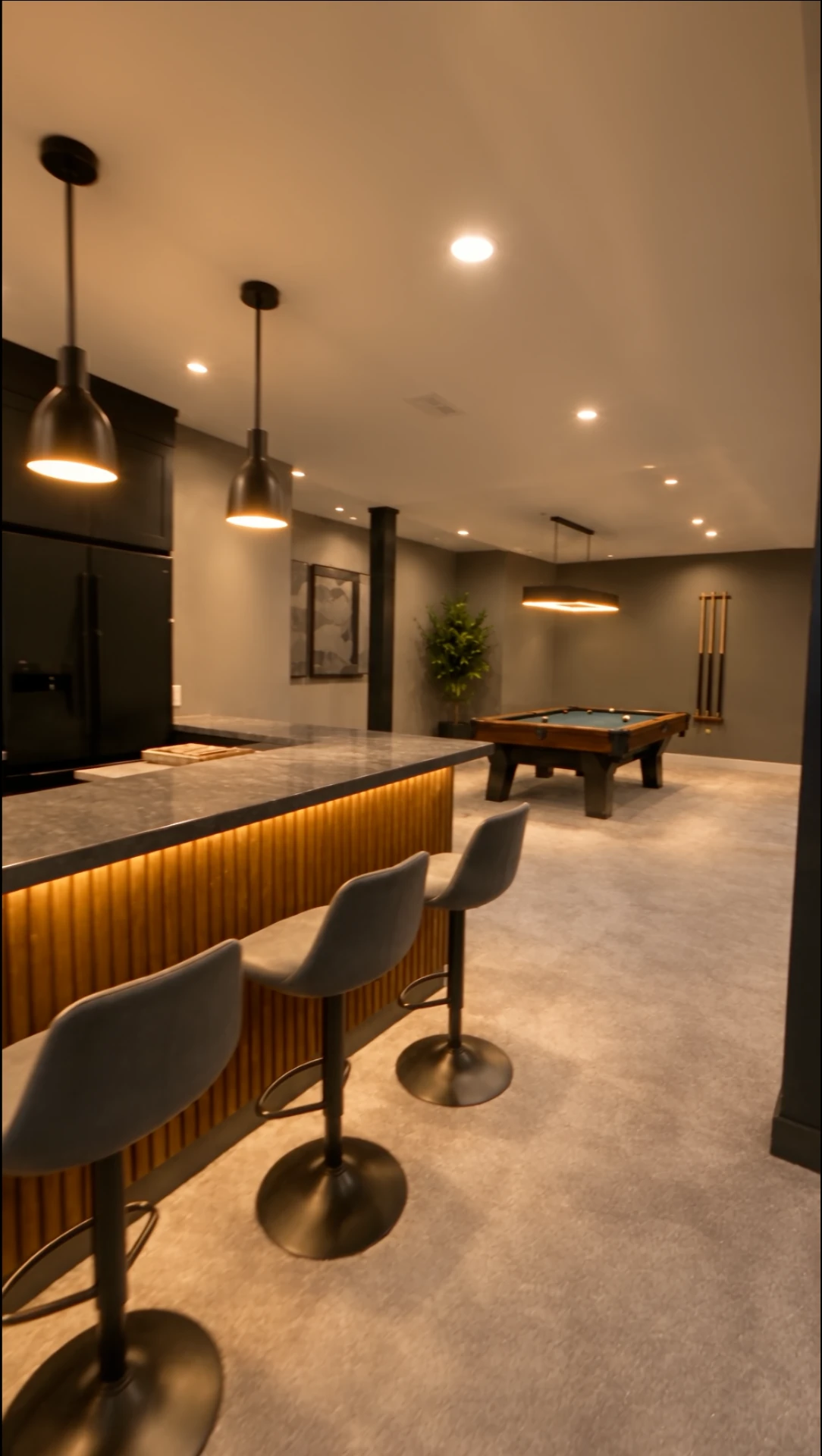 Basement bar with lit wood slat front, stone counter, and barstools facing the game area